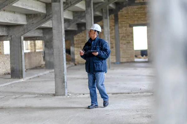 Senior construction manager controlling building site. He is holding tablet in his hands.