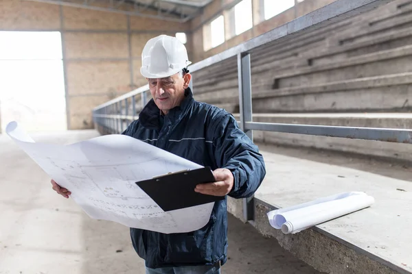 Senior construction manager controlling building site with blueprints.