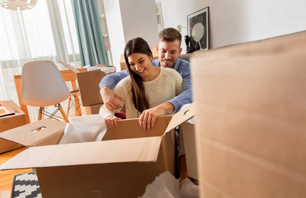 Smiling young couple move into a new home carrying boxes of belongings.