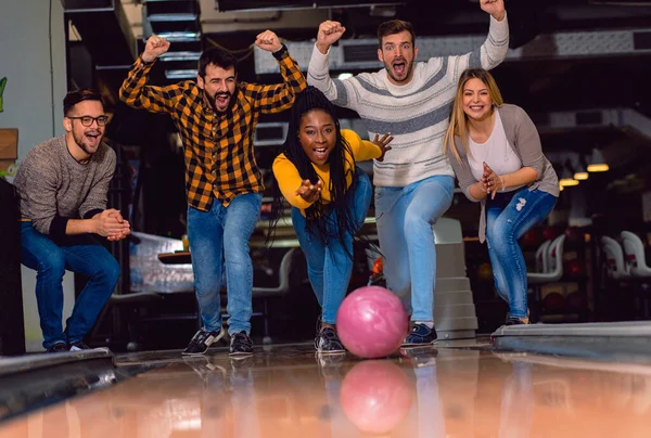 Group of friends enjoying time together laughing and cheering while bowling at club.