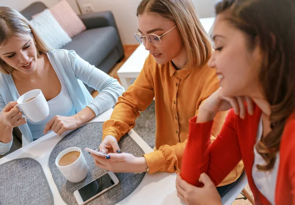 Three female friends enjoy talking while drinking coffee in the morning at home.