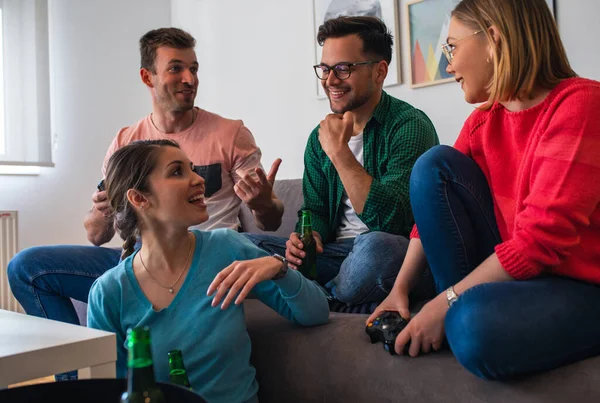 Group of friends having fun sitting on sofa in living room and playing video games at home.