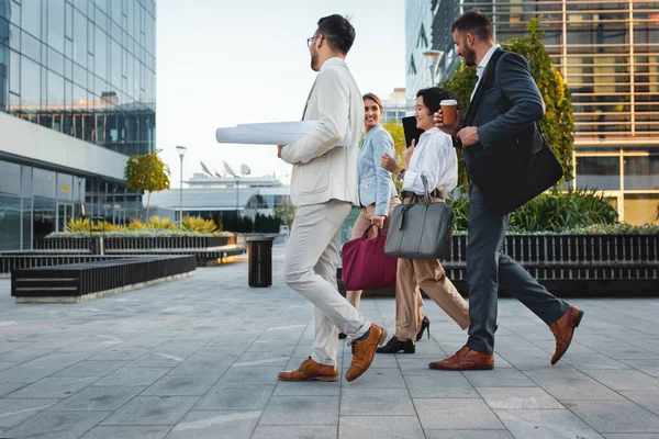 Group of coworkers walking outside in front of office buildings discuss business plan.