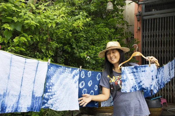 Thai women tie batik dyeing handkerchief tie batik indigo color or mauhom color and hanging process dry clothes in the sun at garden outdoor in Nonthaburi, Thailand