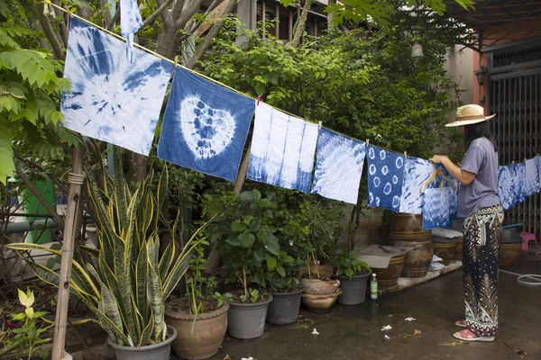 Thai women tie batik dyeing handkerchief tie batik indigo color or mauhom color and hanging process dry clothes in the sun at garden outdoor in Nonthaburi, Thailand