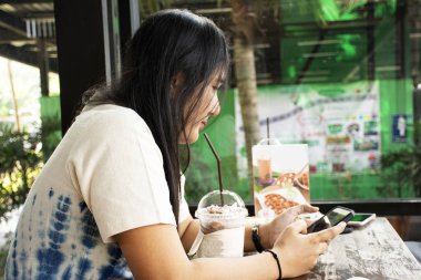 Taylandlı kadın rahat smartphone oynamak ve üzerinde 13 Kasım 2018: Saraburi, Thailand içinde frappe kahve dükkanında çikolata içme otururken