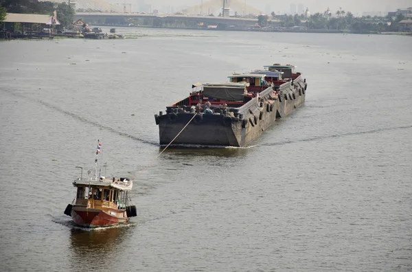 Asian thai people sailing barge and tugboat cargo ship in Chao Phraya or chaopraya river from Bangkok go to Ayutthaya at Phra Nang Klao bridge in Nonthaburi, Thailand