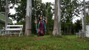 Taylandlı kadın rahatlayıp, Thailand 'ın Ratchaburi Eyaleti' ndeki Ban Pong 'daki Mae Khlong ya da Meklong nehrinin kıyısındaki tatil köyünün bahçesindeki ahşap salıncaklarda oynuyor.