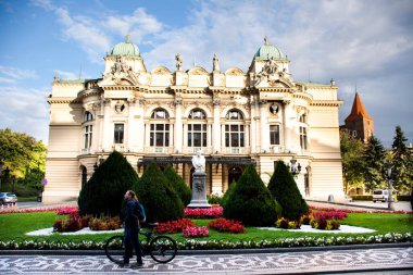 Polonyalı erkekler ve Polonyalı kadınlar bisikletle yürüyen ve iten insanlar 20 Eylül 2019 'da Polonya' nın Lesser kentinde Stare Miasto 'daki Krakow Eski Şehir Meydanı' ndaki Julio Slowacki tiyatrosunun bahçesinden geçtiler.