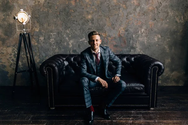 young man in a suit sitting on a sofa smiling