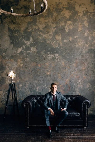 young man in a suit sitting on a sofa smiling