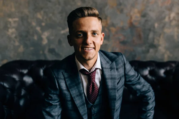 young man in a suit sitting on a sofa smiling