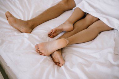 Beyaz çarşaf üzerinde erkek ve kadının bacakları kısmen örtülü b