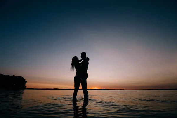 Para całuje na plaży z pięknym zachodzie słońca w oświetlenie tła — Zdjęcie stockowe
