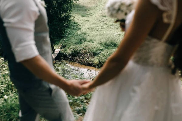 裁剪拍摄美丽的年轻婚礼夫妇手牵手 站在一起附近的小溪 — 图库照片