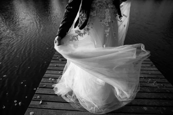 低段年轻的新娘在婚纱和皮夹克在河边的木制走道 黑白图像 — 图库照片