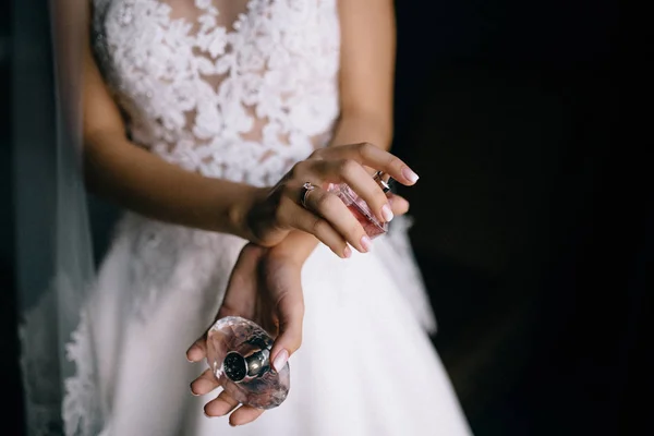 室内に香水瓶を保持する白いウェディングドレスの若い花嫁の中間セクション — ストック写真