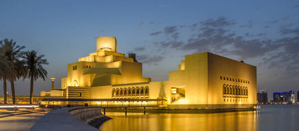Doha,Qatar -November 5,2017:Museum of Islamic Art, Doha, Qatar at night exterior view with light reflection in the Arabic gulf with trees and skyscrapers in the background.