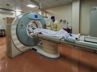Radyoloji Bölümü 'nde kişisel koruyucu ekipman (PPE) giyen radyoloji teknisyeninin COVID-19 hastasını muayene için hazırladığı hesaplanmış tomografi makinesi (CT)