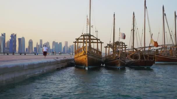 卡塔尔多哈7月4日至2020年7月4日 多哈小生境日落镜头 画面中的独木舟在阿拉伯湾 卡塔尔国旗在前方飘扬 人们在走路 背景是多哈天际线 — 图库视频影像