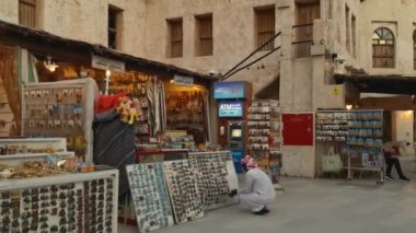 Souq Waqif (Doha, Katar-23 Temmuz 2020) Günbatımında ana caddede geleneksel antikacılar, kahve dükkanları, yürüyen insanlar ve Katar bayrağını gösteriyor 