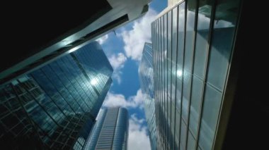 Şehir ufuk çizgisi binaları, mavi gökyüzü ve cam aynalı cephelerin düşük açılı görüntüsü.