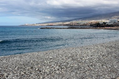 Playa de Las Americas 'taki taşlı plaj. Kanarya adasında. Mavi suyu ve mavi gökyüzü olan tenerife.