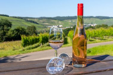 Wine bottle with glasses on wooden table with landscape on river moselle in background clipart