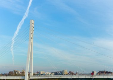 Destek yapısına sahip bir yaya köprüsü, çelik kablolardan oluşan dikey bir kule, açık mavi gökyüzüne karşı.