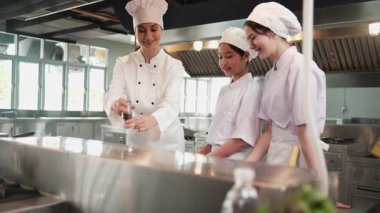 Kadın şef stajyer öğrencilere, yemek pişirme kursuna, yemek pişirme mutfağında profesyonel gurme ustasına lezzetli yemekler pişirmede malzeme hazırlama ve aşçı yemeklerine gösteri yapıyor..