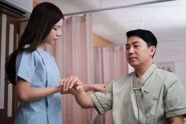 Asyalı erkek hasta el germe, kas ağrısı tedavisi için kadın fizyoterapist tarafından tedavi, kaplıca kliniğinde pasif tıbbi terapi ve sağlık masajı..