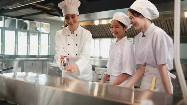 Kadın şef stajyer öğrencilere, yemek pişirme kursuna, yemek pişirme mutfağında profesyonel gurme ustasına lezzetli yemekler pişirmede malzeme hazırlama ve aşçı yemeklerine gösteri yapıyor..