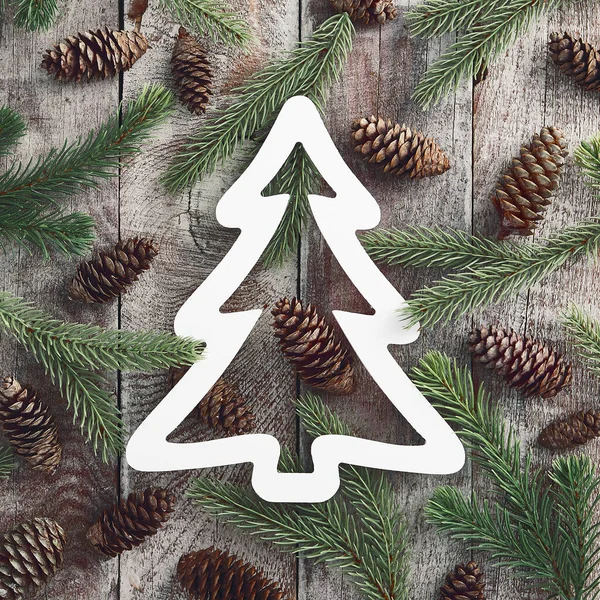 Rustic wooden texture with tree shaped paper frame. Old timber panels. Fir tree branches and pine cones on shabby barn floor. Winter season background. Christmas backdrop. Greeting card design idea