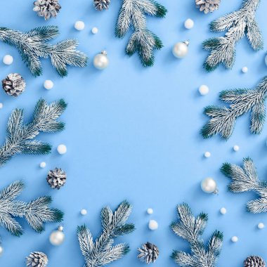 Noel asgari konsepti - klasik mavi arka planda karlı Noel süslemesi. Çam dalı ve koni, takı ve soyut kartopu. Kare kompozisyon, düz yatış. Merkezi kopyalama alanı