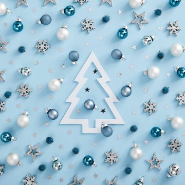 Minimum Noel modeli - beyaz, gümüş ve mavi toplar, kar taneleri ve mavi arka planda yıldızlar. Kare kompozisyon, düz döşeme, üst manzara. Kağıt noel ağacı siluetiyle soğuk monokrom düzeni
