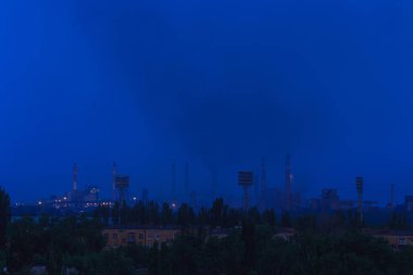 Şehrin kenar mahallelerinde ağır ağır sigara içen büyük bir metal bitkisinin panoraması.