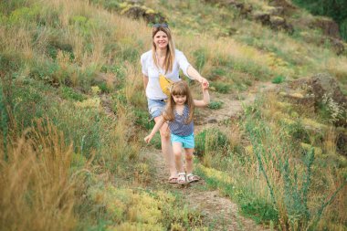 Anne ve kızı kayalık yamaçta el ele yürür.