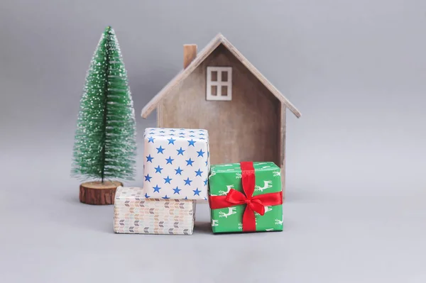 Wooden small house with gifts and Christmas tree against gray background. New Year\'s composition. Christmas presents.