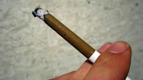 Cigarrillo ardiente en la mano en el fondo de la pared — Foto de Stock