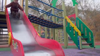 Mutlu küçük çocuk parkta oynuyor, kayaktan kayıyor ve bir tur daha koşuyor.