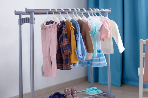 Pasztell színű gyermekruhák egy sorban a nyitott akasztón beltérben. Ruhák kis hölgyeknek a gyerekszobában.. — Stock Fotó