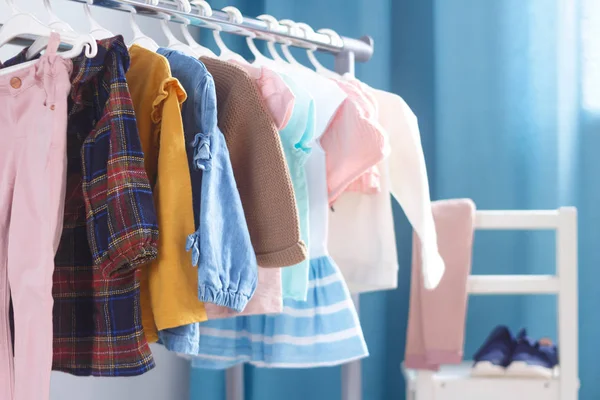 Pasztell színű gyermekruhák egy sorban a nyitott akasztón beltérben. Ruhák kis hölgyeknek a gyerekszobában.. — Stock Fotó