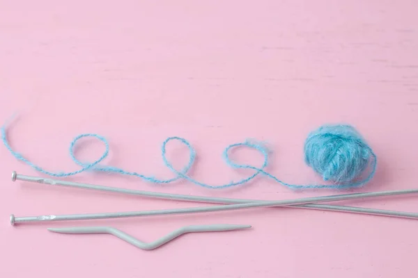 Una pequeña madeja azul de lana mohair se encuentra en la superficie rosa junto a las agujas de tejer el hilo está enroscado — Foto de Stock