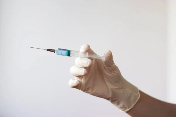 A rubber gloved hand holds a syringe with a needle filled with a blue liquid.