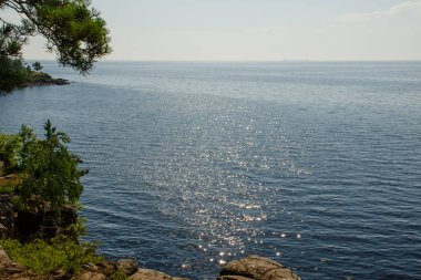 Mavi göl suyu güneşte parlar, uçurumdaki orman ve mavi yaz gökyüzü