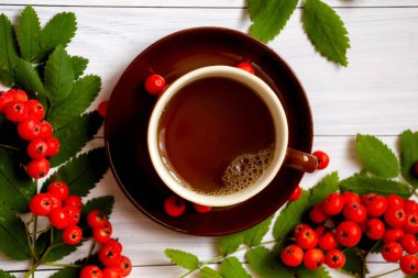 Beyaz bir masada kahverengi bir fincan sıcak çay ve yaban mersini. Sonbahar düzlüğü.