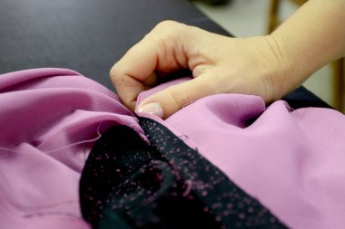 Terzi elbise dikmek için örgü hazırlar. Kadın elleri dikiş masasının üzerine siyah ve pembe kumaş seriyor. Küçük işletme.