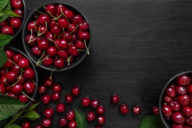 Siyah bir masada yeşil yapraklı kırmızı kiraz.