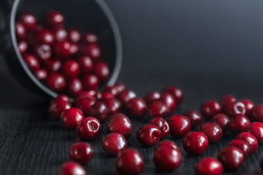 Olgun kırmızı kiraz, siyah bir masanın üzerindeki koyu bir tabaktan kırılır.