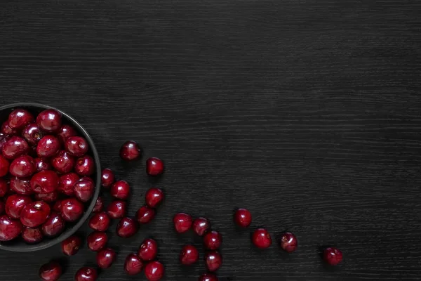 Cerise rouge avec des feuilles vertes dans une assiette sombre sur une table noire — Photo